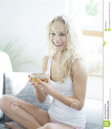 Young Woman Holding Herbal Tea Cup While Sitting On Sofa Stock Photo
