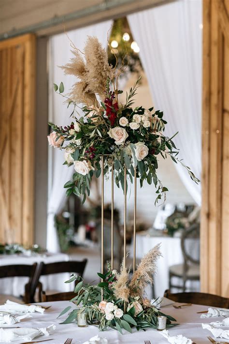 A Tall Centerpiece With Flowers And Greenery On A Table