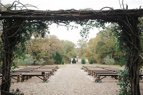 An Outdoor Ceremony Setup With Wooden Benches And Vines On The Arbors