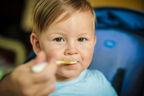 Beautiful Happy Baby Boy Eating Porridge Food With A Spoon Stock Photo