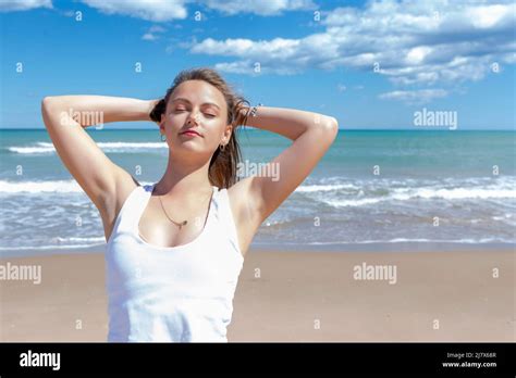 mujer rubia en la playa estirando con los brazos detrás de su cabeza y los ojos cerrados