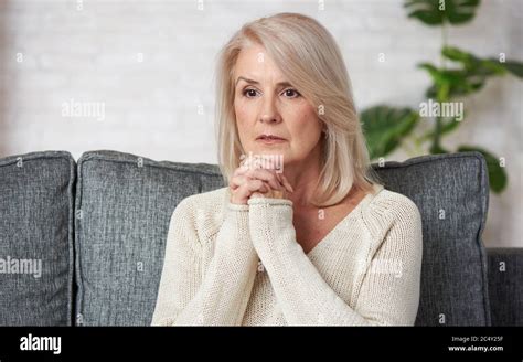 Portrait Of Sad Mature Woman Sitting On Couch At Home And Looking Away