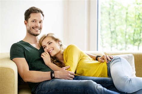 Couple Sitting On Couch In Their New Home Cuddling Stock Photo