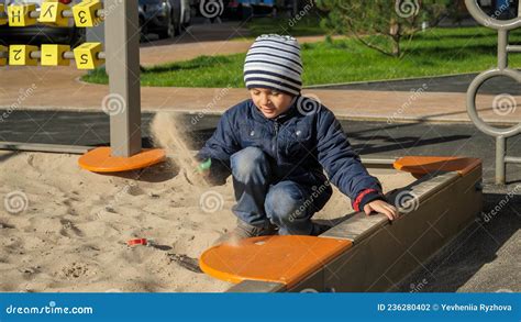 Little Boy Playing In Sandbox On Playground In Park And Digging Sand