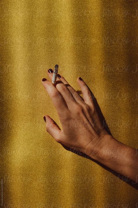 Womans Hand Holding A Cigarette On A Golden Background Del