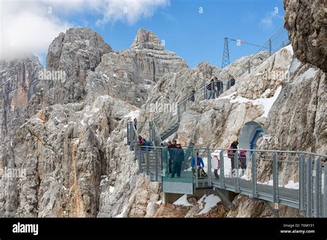 Austrian Dachstein Mountains With Hikers Passing A Skywalk Rope Bridge