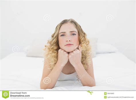 Pretty Frowning Blonde Lying On Bed Looking At Camera Stock Image