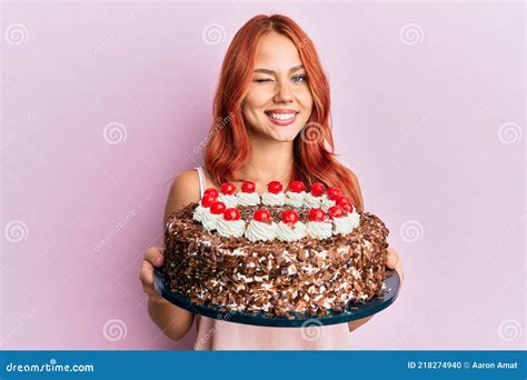 Young Redhead Woman Celebrating Birthday With Cake Winking Looking At