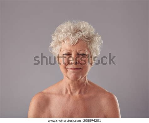 Portrait Of Beautiful Naked Senior Woman Looking Happy Against Grey