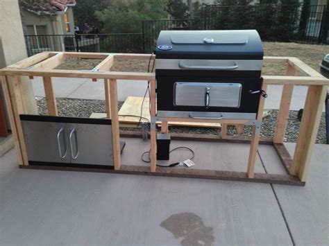 An Outdoor Grill Built Into The Side Of A House With Wood Framing Around It And Two Ovens On