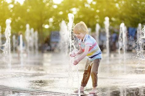 Little Boy Plays In The Square Between The Water Jets In The Fountain