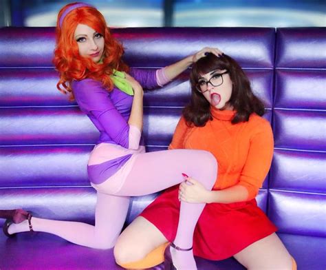 Two Women Dressed In Costumes Sitting On A Purple Couch And Posing For