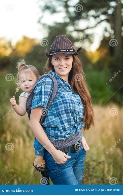 Cowgirl Mother Carrying Her Small Daughter In A Baby Sling Stock Photo