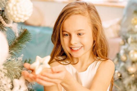 A Cute Little Girl In A White Dress Holds A Christmas Tree Toy In Her