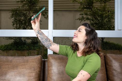 Brazilian Tattooed Woman Making Selfie Sitting On The Brown Sofa Stock