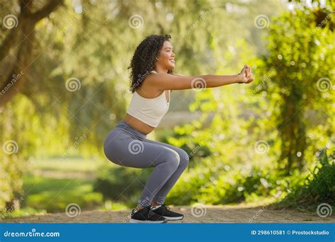 Side View Of Fitness Woman Enjoys Outdoor Workout While Squats Stock