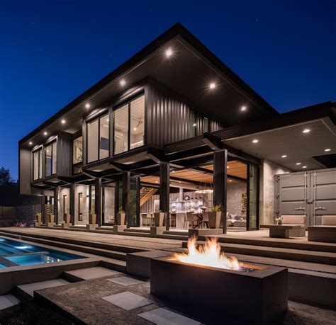 A Modern House With A Fire Pit In The Front Yard At Night Lit Up By