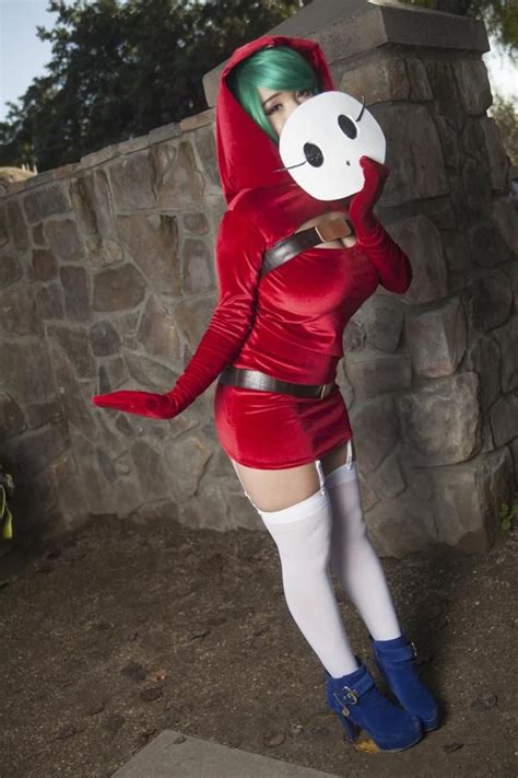 A Woman In A Red Dress And White Mask Poses For The Camera With Her Hands On Her Hips