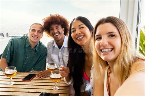 Multiracial Group Of Friends Taking Selfie Looking At Camera While Having Drinks Together At