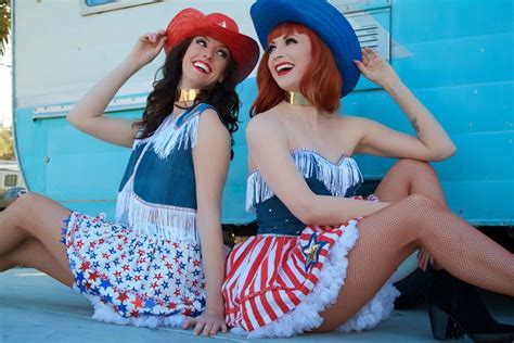 Two Women Dressed In Patriotic Clothing Sitting On The Ground Next To A Blue Bus And One Is