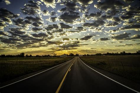 Paved Road Leading Into The Horizon As Sun Rays Beam Out Of The Clouds