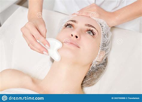 Beautician Making Facial Massage With Gua Sha Stone Of Woman Face Skin For Lymphatic Drainage
