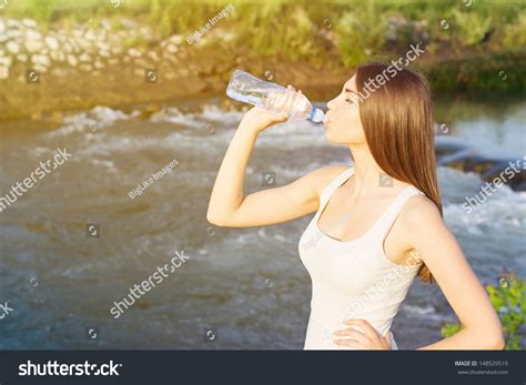 Tired Young Woman Drinking Water After Running By The River Stock Photo
