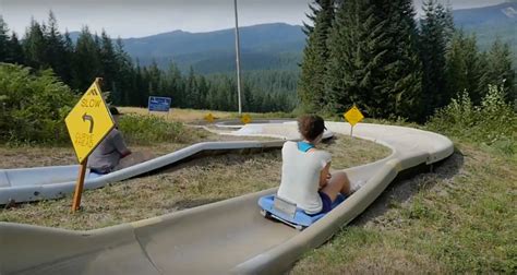 Two People Are Sitting On A Slide At The Top Of A Hill