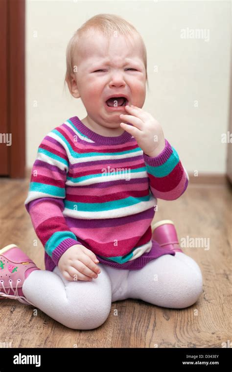 Portrait Of Crying Baby Girl In Purple Dress On Living Room Stock Photo