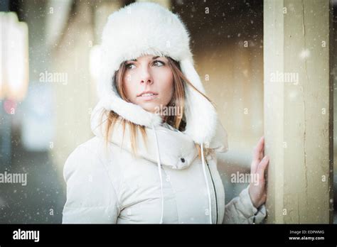 Young Woman In Fur Hat And Down Jacket Under Falling Snow Stock Photo