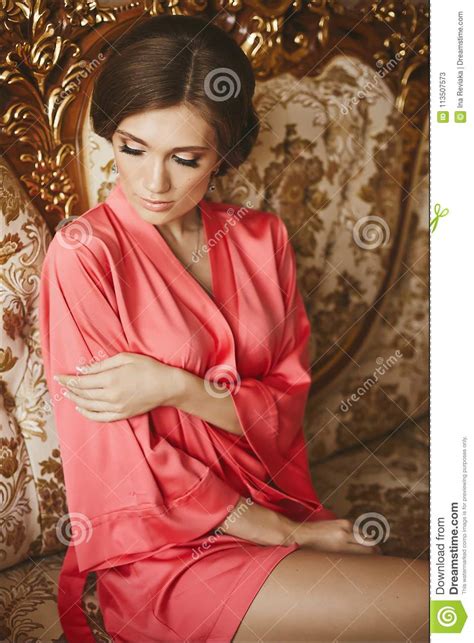 Beautiful And Brunette Model Girl In Peignoir Posing On Sofa At Luxury Interior Stock Image