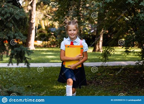 Happy Schoolgirl Holding A Book Outdoors A Small Child Goes To School