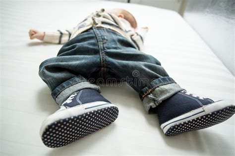 Closeup Of Baby Boy Feet In Jeans And Sneakers Lying On Bed Stock Photo