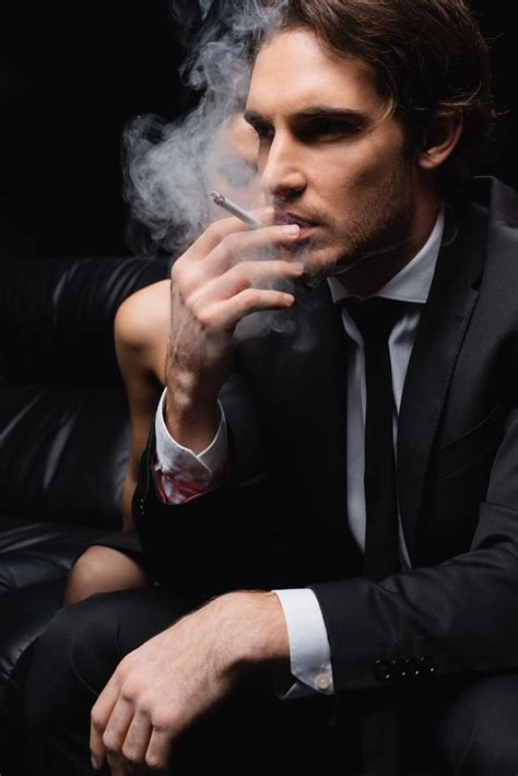 Serious Man In Suit Smoking Cigarette Near Woman On Blurred Black
