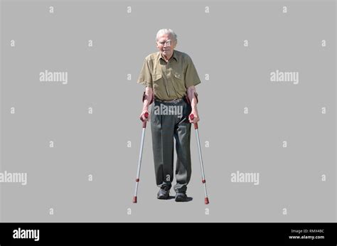 Senior Retired Man Walking On Crutches On A Walkway Between Green