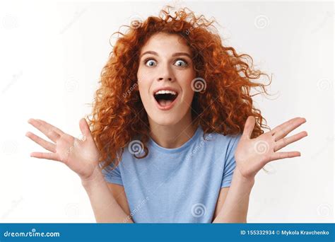 close up shot emotive attractive redhead curly haired woman raising hands up surprised and