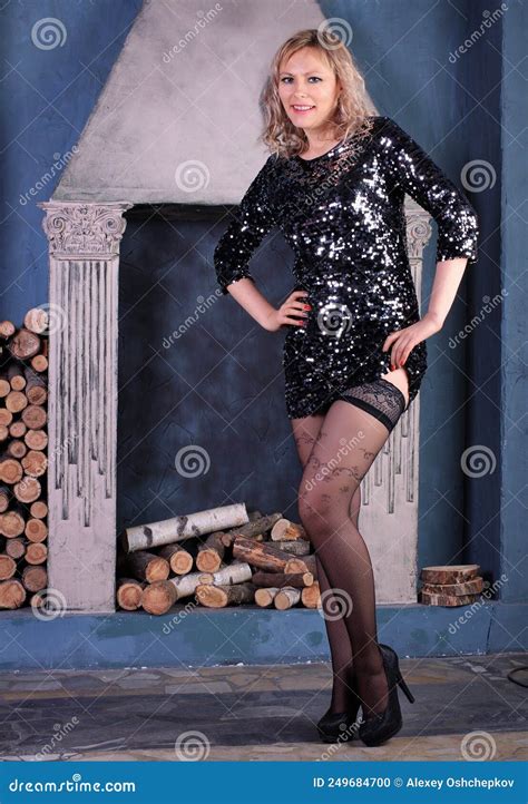 Beautiful Long Legged Blonde Girl In Black Dress And Black Stockings Posing At Fireplace Stock