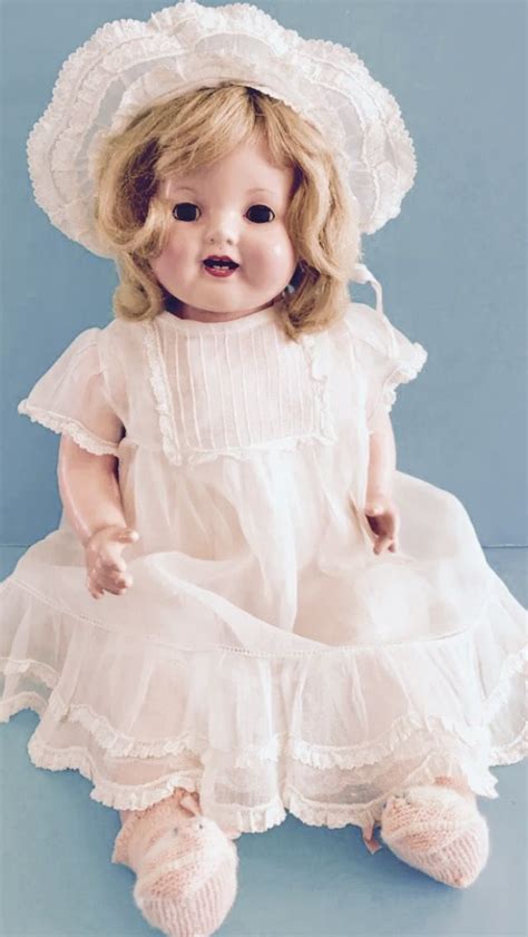 A Porcelain Doll Wearing A White Dress And Hat