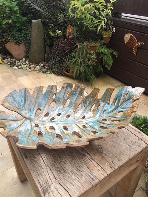 A Large Metal Leaf Bowl Sitting On Top Of A Wooden Table Next To Potted