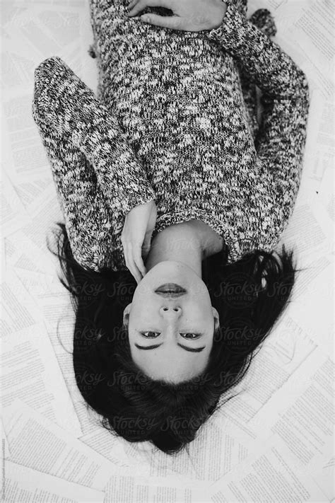 Young Black Haired Woman Lying Down On Pages Of A Book By Stocksy