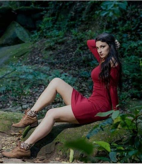 A Woman In A Red Dress Is Sitting On A Rock And Posing For The Camera