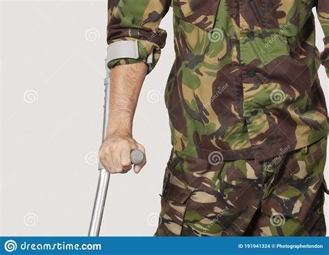 Mid Section Of Young Soldier Holding Crutches Against Gray Background