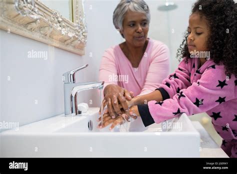 Grandmother And Granddaughter Washing Hands In Bathroom Sink At Home