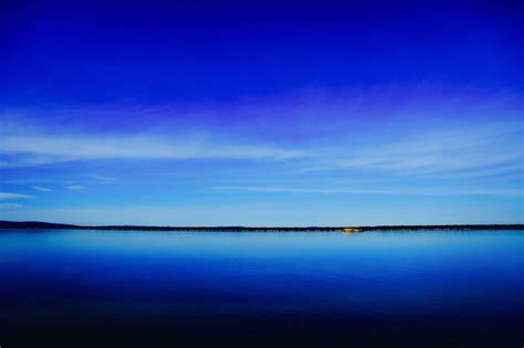 A Deep Blue Lake And Clear Sky Separated By A Dark Green Shoreline On