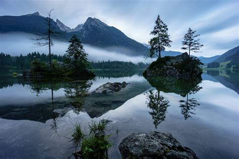 Two Islets With Two Trees Surrounded By Water Near Fog Covered Mountain