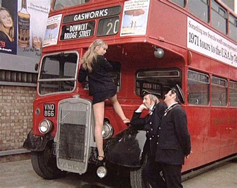 A Woman Standing On The Back Of A Red Double Decker Bus While Two Men Stand Next To It