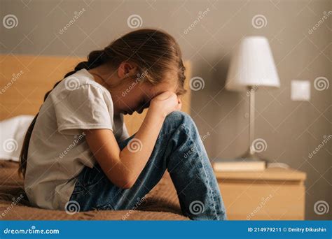 Side View Of Sad Little Girl Hugging Knee Sobbing With Head Bowed And