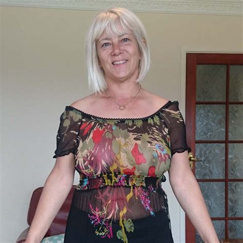 A Woman With White Hair Is Standing In Front Of A Cake And Smiling At The Camera