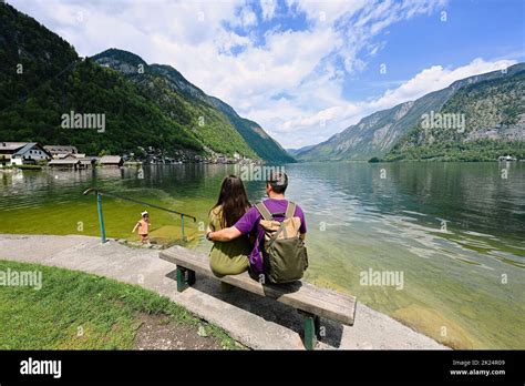 Couple With Baby Girl Sitting On Bench Over Austrian Alps Lake In