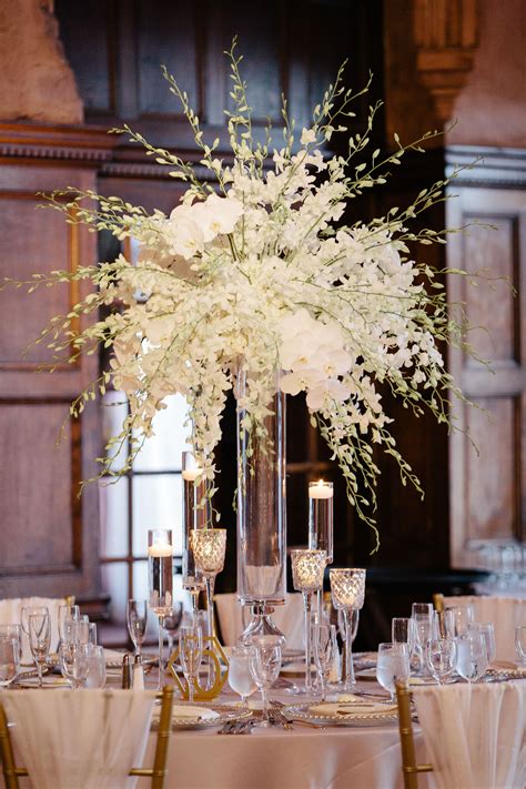 A Tall Vase Filled With White Flowers Sitting On Top Of A Table Covered